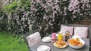 A metal table set outdoors with plates, a bowl of fruit, a bottle of juice, and a pitcher of coffee. - The House On The Green (Chipping Norton)
