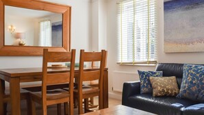 A dining area with a wooden table and chairs, a large mirror, and a view of the city through a window with blinds. - The House On The Green (Chipping Norton)