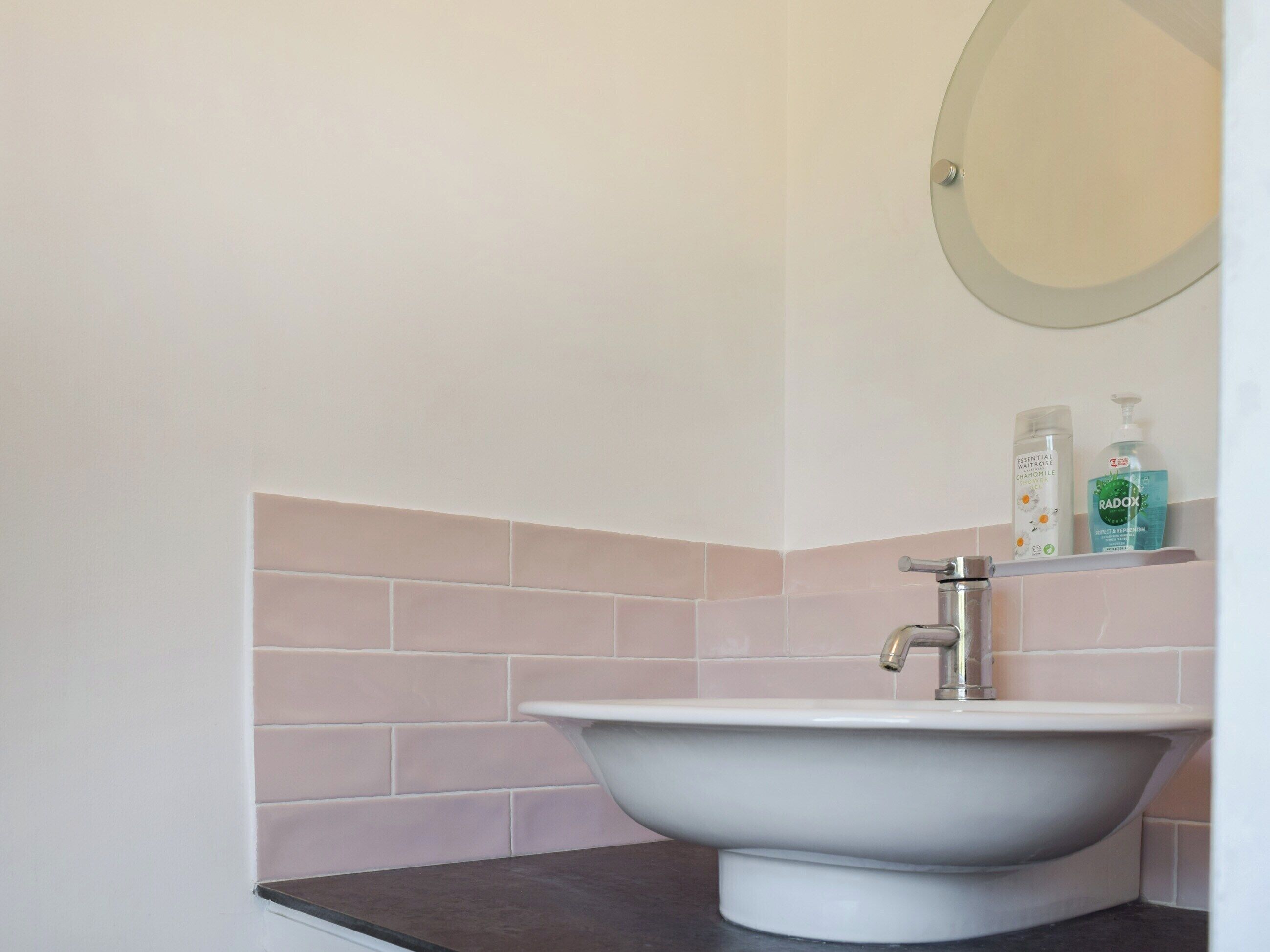 Une salle de bain avec un lavabo blanc, un miroir et une étagère contenant des articles de toilette.