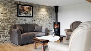 A cozy living room with a stone wall, a sofa, a chair, a table with glasses, and a wood-burning stove. - 2 bedroom accommodation in Felindre, near Swansea (Felindre, near Swansea)