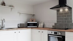 A modern kitchen with white cabinets, a stainless steel range hood, a microwave, a toaster, and a built-in oven. - 2 bedroom accommodation in Felindre, near Swansea (Felindre, near Swansea)