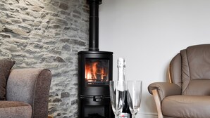 A cozy living room with a stone wall, a black wood-burning stove, a leather sofa, and a bottle of Martini wine on a table. - 2 bedroom accommodation in Felindre, near Swansea (Felindre, near Swansea)
