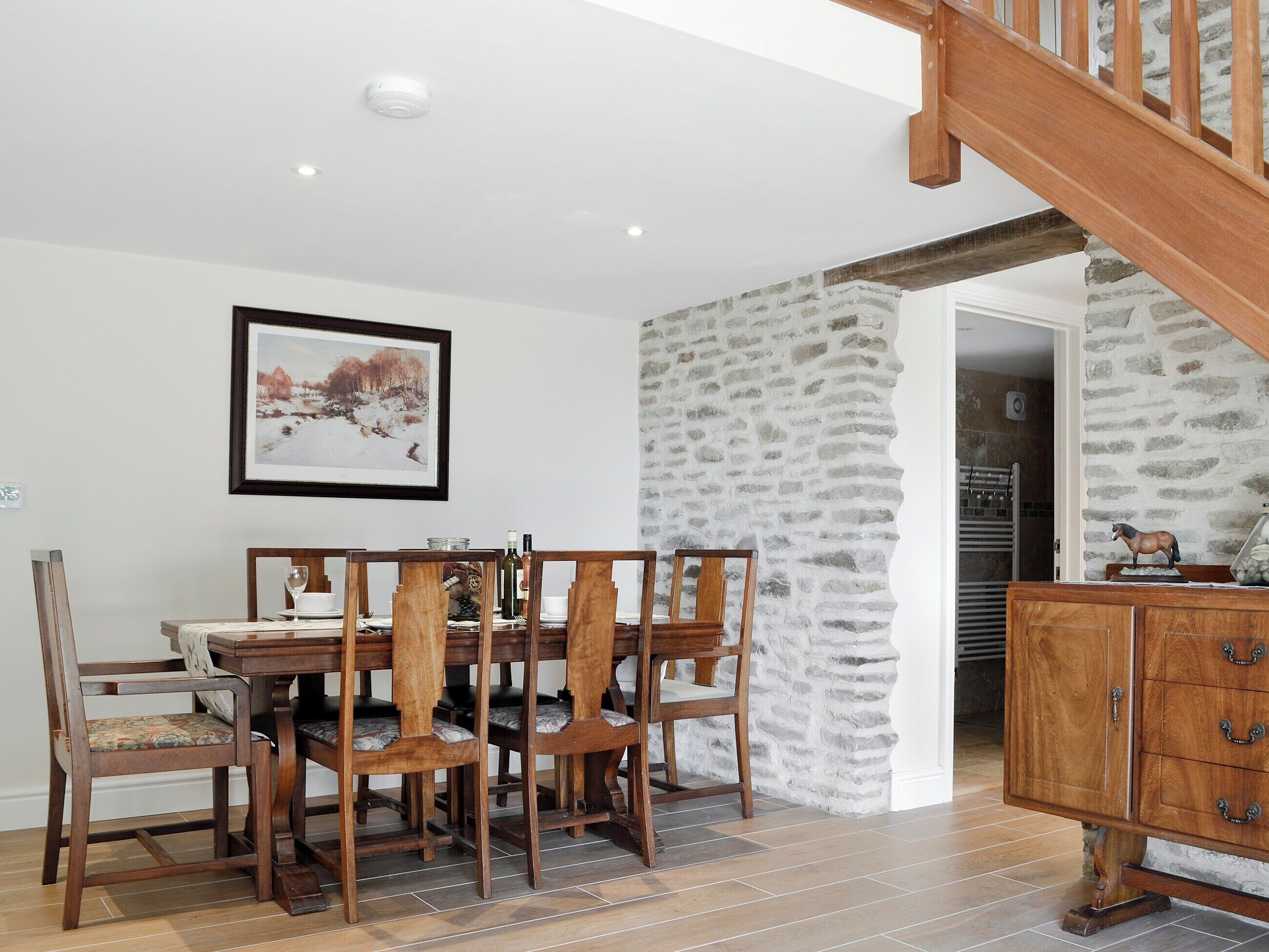 A dining area with a wooden table and chairs, a stone wall, and a staircase.
