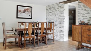 A dining area with a wooden table and chairs, a stone wall, and a staircase. - 2 bedroom accommodation in Felindre, near Swansea (Felindre, near Swansea)