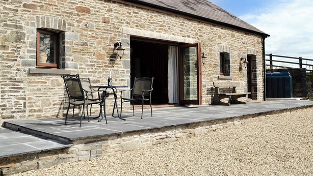 A stone building with a patio area featuring a table and chairs, a wooden bench, and a stone wall. - 2 bedroom accommodation in Felindre, near Swansea (Felindre, near Swansea)