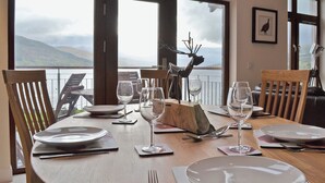 Une table à manger dressée pour quatre personnes, avec des verres à vin et des assiettes, offrant une vue panoramique sur un magnifique lac.