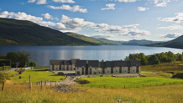 Un hôtel situé au bord d’un lac, composé de plusieurs bâtiments, doté d’une pelouse verdoyante et offrant une vue sur le lac et les montagnes.