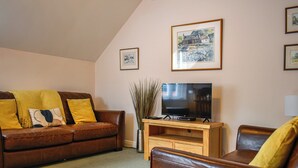 A living room with a brown leather sofa, a wooden TV stand, and a large framed picture on the wall. - 2 bedroom accommodation in Whitby (Whitby)