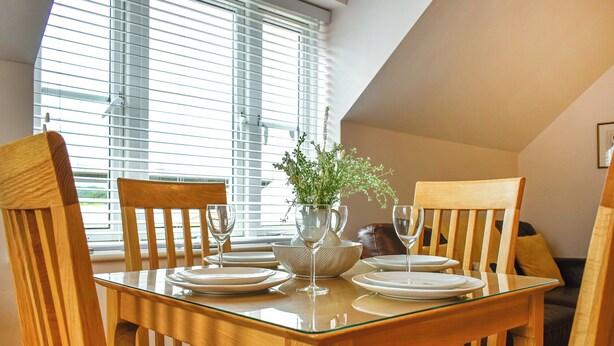 A dining area with a glass-top table, wooden chairs, and a vase with greenery. - 2 bedroom accommodation in Whitby (Whitby)