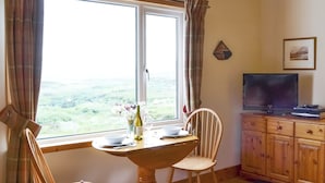 Un comedor con una mesa, sillas, un televisor y vistas al campo.