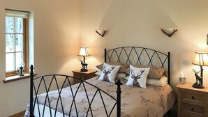 Une chambre à coucher comprenant un lit, deux tables de chevet, une fenêtre et une paire de bois de cerf fixée au mur.
