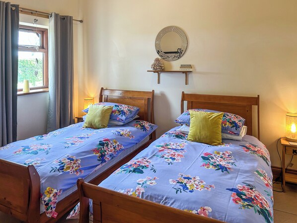 A bedroom with two wooden beds, floral bedding, a round mirror, and a small shelf with books. - 2 bedroom accommodation in Mumby, near Anderby Creek (Mumby, near Anderby Creek)