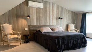A modern bedroom with a large bed, two chairs, a small table, and an air conditioning unit on the wall. - B&B Silentium (Tielt-Winge)