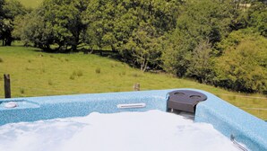Uma banheira de hidromassagem com exterior azul texturizado, rodeada por um campo gramado e árvores.