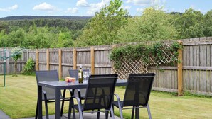 An outdoor patio with a table and chairs, a bottle of wine, and a fruit bowl. - 4 bedroom accommodation in Aviemore (Aviemore)