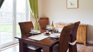 A dining area with a table set for four, including wine glasses, plates, and a bottle of wine. There are wicker chairs and a wooden cabinet in the background. - 4 bedroom accommodation in Aviemore (Aviemore)