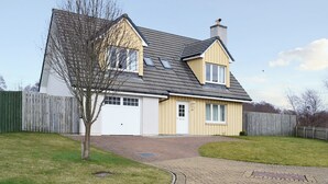 A two-story house with a garage, a chimney, and a paved driveway. - 4 bedroom accommodation in Aviemore (Aviemore)