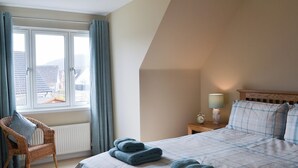 A bedroom with a bed, a chair, a nightstand, a lamp, and a window with curtains. - 4 bedroom accommodation in Aviemore (Aviemore)