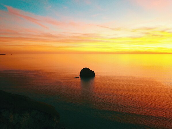 A coastal landscape with a prominent rock formation in the sea, a distant shoreline, and a clear sky. - 2 bedroom accommodation in Trebarwith, Delabole (Trebarwith, Delabole)