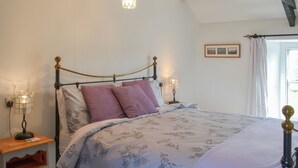 A bedroom with a bed, two bedside lamps, a nightstand, a wooden cabinet, and a window with curtains. - 2 bedroom accommodation in Trebarwith, Delabole (Trebarwith, Delabole)