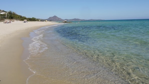 Une plage avec une eau claire et peu profonde, un rivage sablonneux et une montagne en arrière-plan.