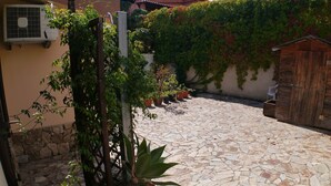 Une cour dallée de pierres, agrémentée de plantes en pot et dotée d’un portail en bois.