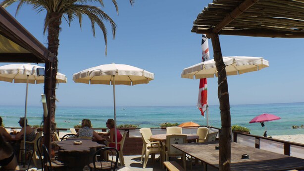 Un espace extérieur aménagé avec des tables, des chaises, des parasols et une vue sur l’océan.
