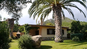 Une maison à l’extérieur en pierre, avec une cheminée en pierre et une pelouse bien entretenue agrémentée de palmiers.