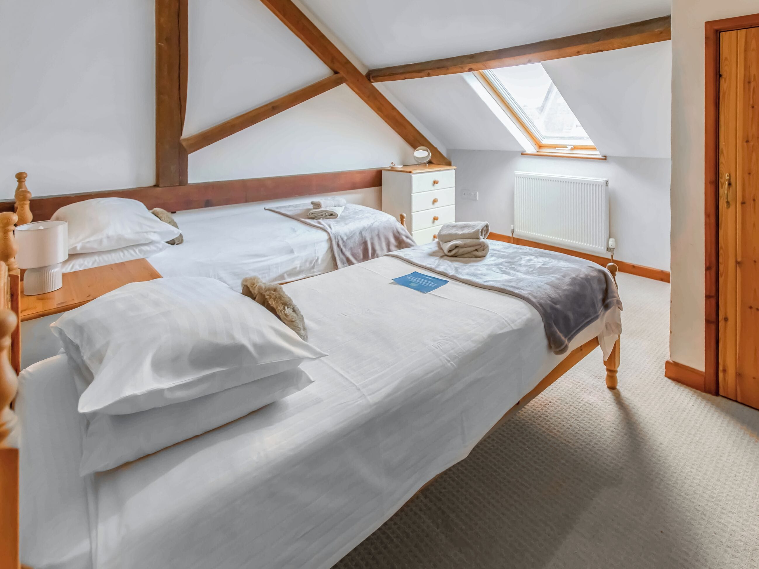 Habitación con dos camas, techo de madera, tragaluz, radiador y puerta de madera.