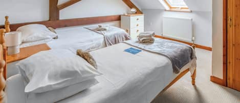 A room with two beds, a wooden ceiling, a skylight, a radiator, and a wooden door.