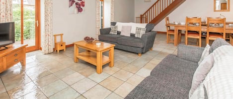 A living room with a sofa, a coffee table, a television, and a dining area with chairs and a table.