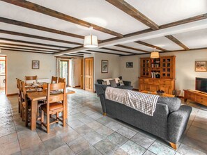 A spacious living area with a dining table, chairs, a sofa, and a wooden cabinet.