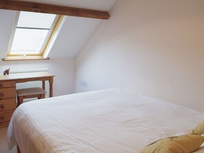 A bedroom with a bed, a desk, a chair, a radiator, and a skylight.