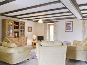 A living room with two beige sofas, a wooden cabinet, a television, and a window with curtains.
