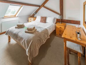 A bedroom with a bed, bedside tables, a wooden nightstand, a desk, and a window.