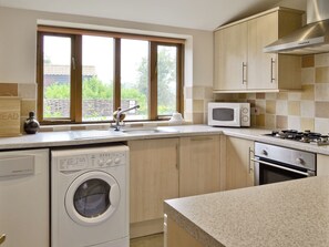 A kitchen with a washing machine, a microwave, a stove, and a window with a view of greenery.