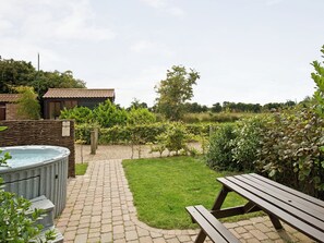 A garden with a hot tub, a picnic table, a brick pathway, and a building with a tiled roof.