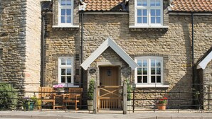 A stone building with a traditional design, featuring a wooden door, two windows with white frames, and a small porch with wooden furniture.
