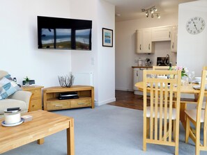 A modern living room with a flat-screen TV, wooden furniture, a dining area with a wooden table and chairs, and a kitchen with white cabinets. - 2 bedroom accommodation in Inverboyndie, near Banff (Inverboyndie, near Banff)