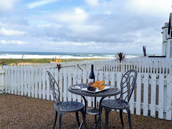 A table with a bottle of wine, a glass, and food, set against a white fence overlooking the ocean. - 2 bedroom accommodation in Inverboyndie, near Banff (Inverboyndie, near Banff)