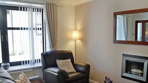 A living room with a black leather sofa, a black leather armchair, a small table with a vase, a floor lamp, and a fireplace. - 2 bedroom accommodation in Moffat (Moffat)