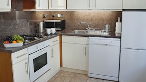 A modern kitchen with white cabinets, a gas stove, a microwave, a sink, and a dishwasher. - 2 bedroom accommodation in Moffat (Moffat)