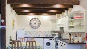 Une cuisine avec des poutres en bois, une horloge, un lave-linge et un four à micro-ondes.