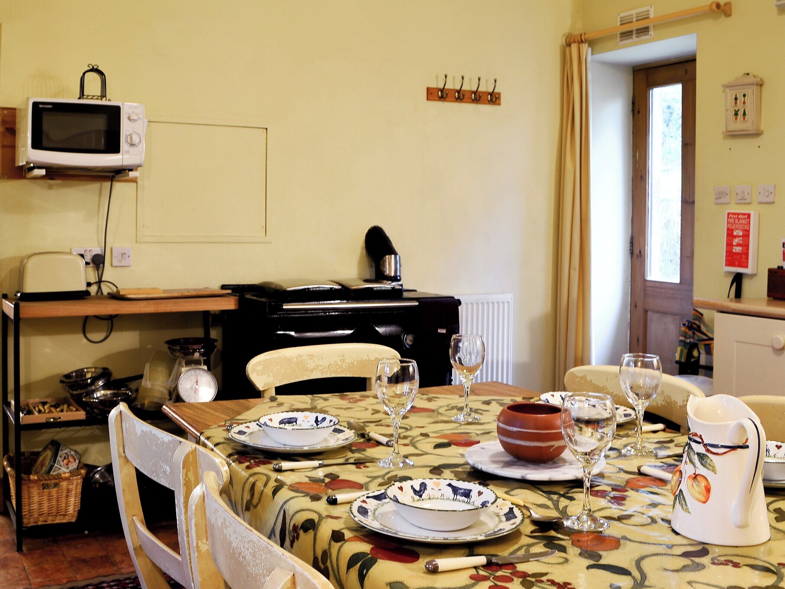 A dining area with a table set for two, a microwave above the table, and a coat rack on the wall.