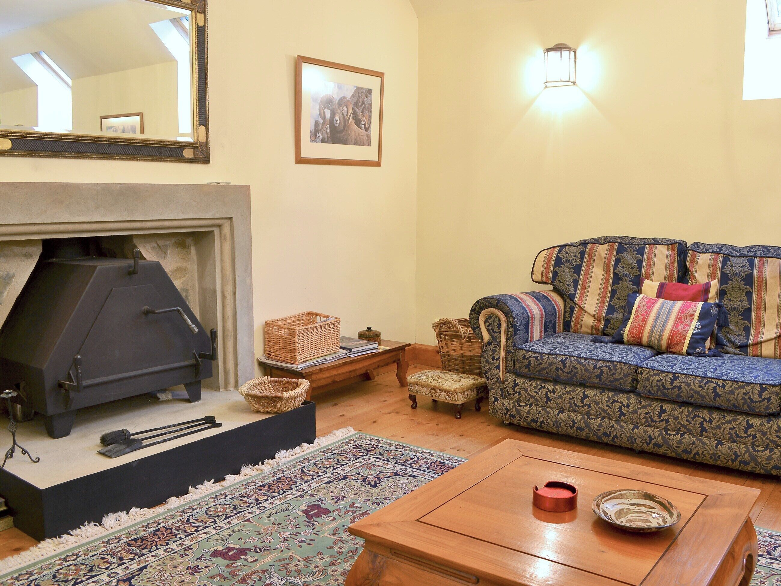 Una sala de estar acogedora con chimenea, un sofá estampado, una mesa de centro de madera y una alfombra decorativa.