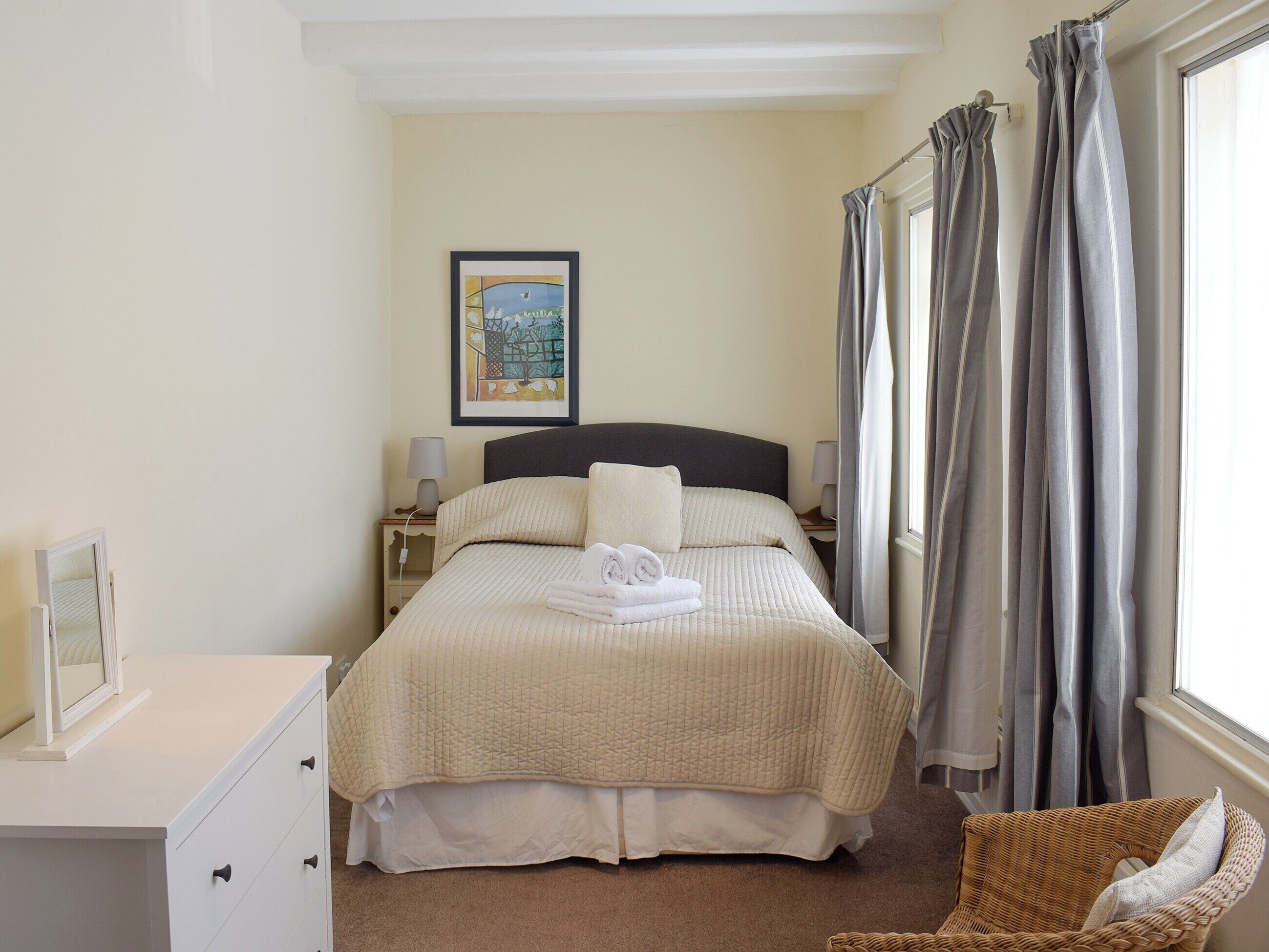 A neatly arranged bedroom with a bed, bedside tables, a chair, and a window with curtains.