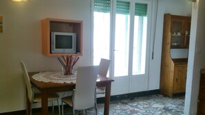 Un comedor con mesa, sillas, un televisor sobre una estantería y un armario.