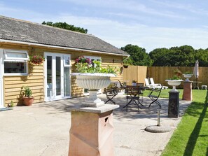 A patio with a table and chairs, a hanging flower pot, and a wooden fence in the background.
