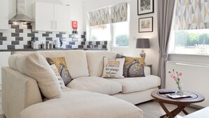 Un soggiorno moderno con un divano modulare beige, un tavolino da caffè rotondo in legno e una cucina sullo sfondo.