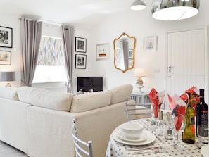 A modern living room with a sofa, dining table set with plates, glasses, and bottles, and a TV on the wall. - 2 bedroom accommodation in Bilsington, near Ashford (Bilsington, near Ashford)